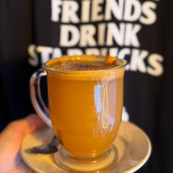 A Brewed Awakening pumpkin spice latte in a clear mug with a spoon on a saucer.