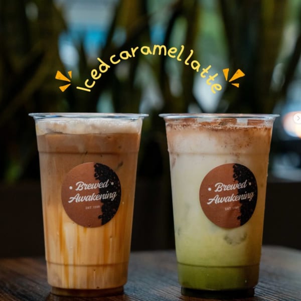 Two Brewed Awakening iced lattes, one caramel and one green, on a dark wooden table.