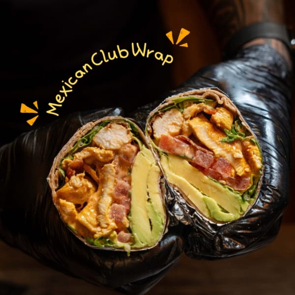 Hands in black gloves holding a sliced Mexican Club Wrap filled with chicken, avocado, and tomatoes.