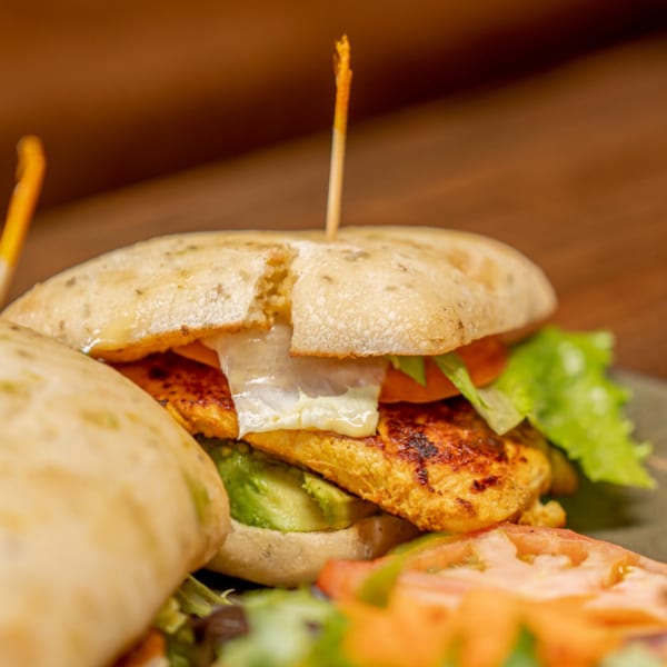 Grilled chicken sandwich with melted cheese, avocado, lettuce, and tomato on a ciabatta bun.